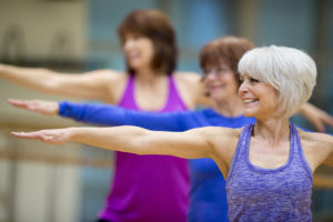 A group of senior adult women are taking a yoga class together at the gym.